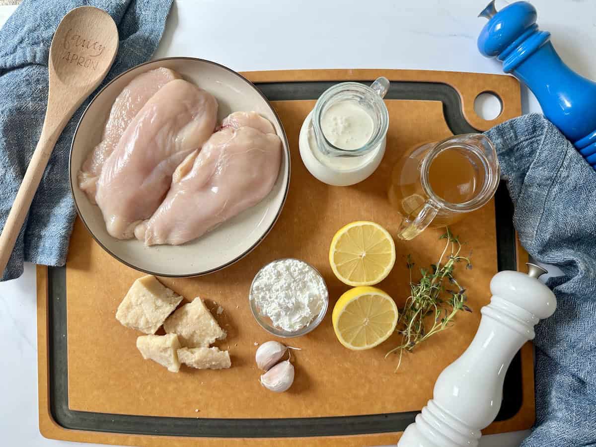 chicken breast cutlets on plate various ingredients in glass bowls on wood cutting board wooden spoon blue linens salt and pepper grinders