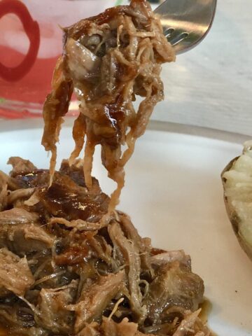 Saucy pulled pork plated with a baked potato and beverage