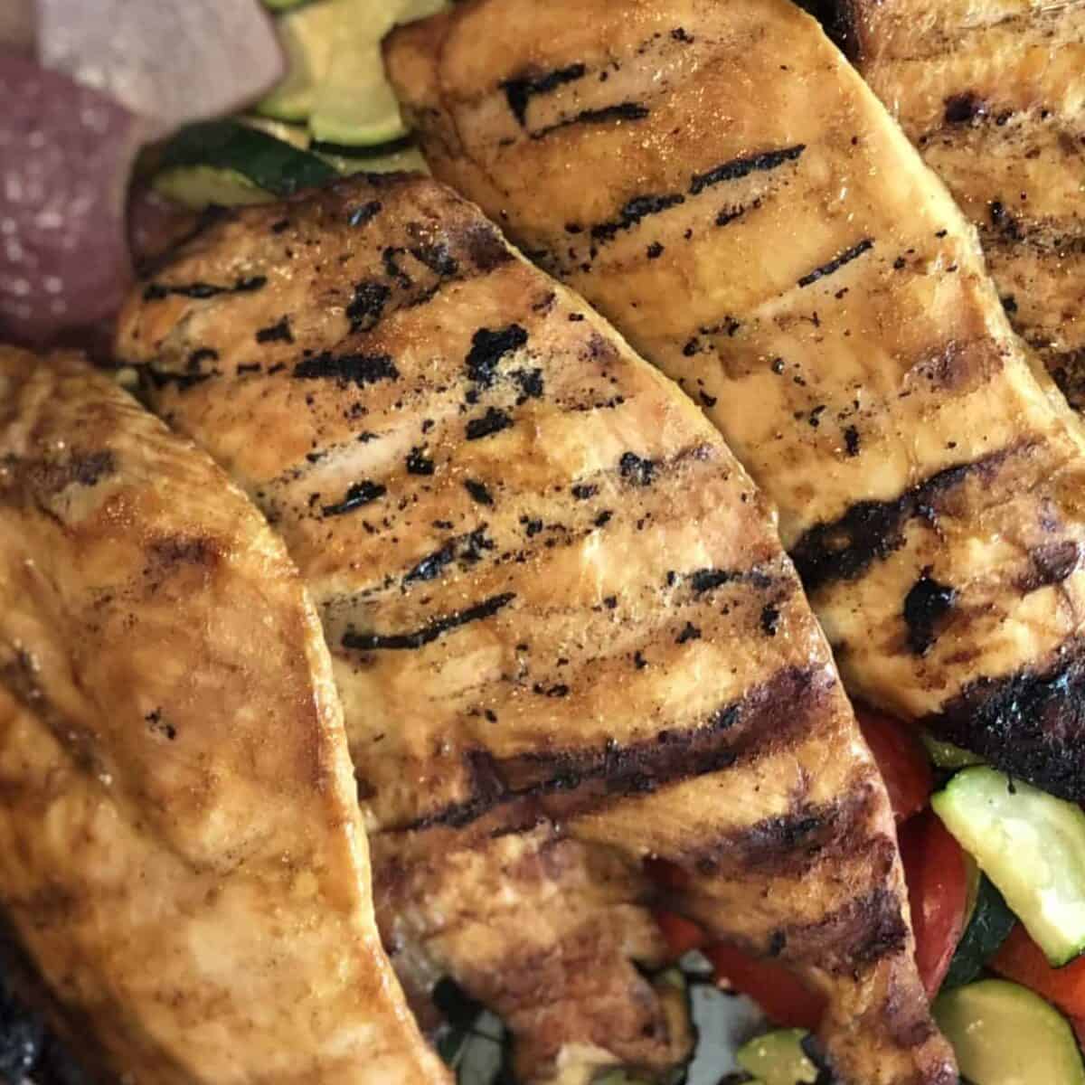 3 chicken breast cutlets on a bed of grilled vegetables including red onion zucchini and red bell pepper