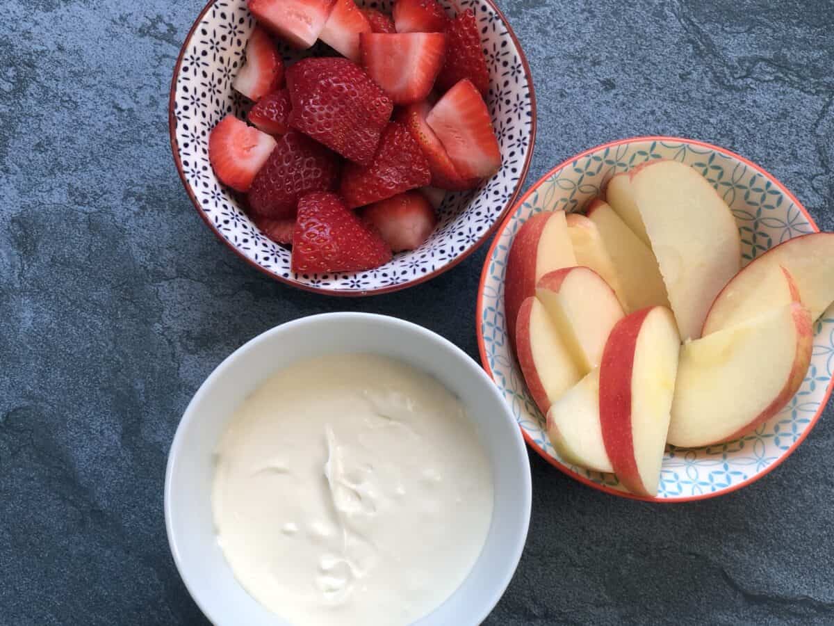 bowl of cheesecake dip with cut strawberries and sliced apples