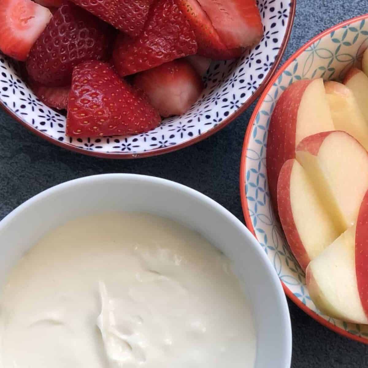 bowl of cheesecake dip with cut strawberries and sliced apples