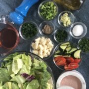 chopped lettuce, herbs, olive oil, vinegar, pepper jack cheese on blue countertop