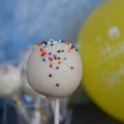 white cake pop with rainbow sprinkles, yellow balloon, and blue background.