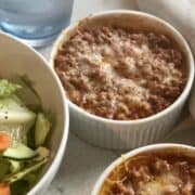 an individual butternut squash lasagna topped with melted cheese a bowl of green salad and glass of water