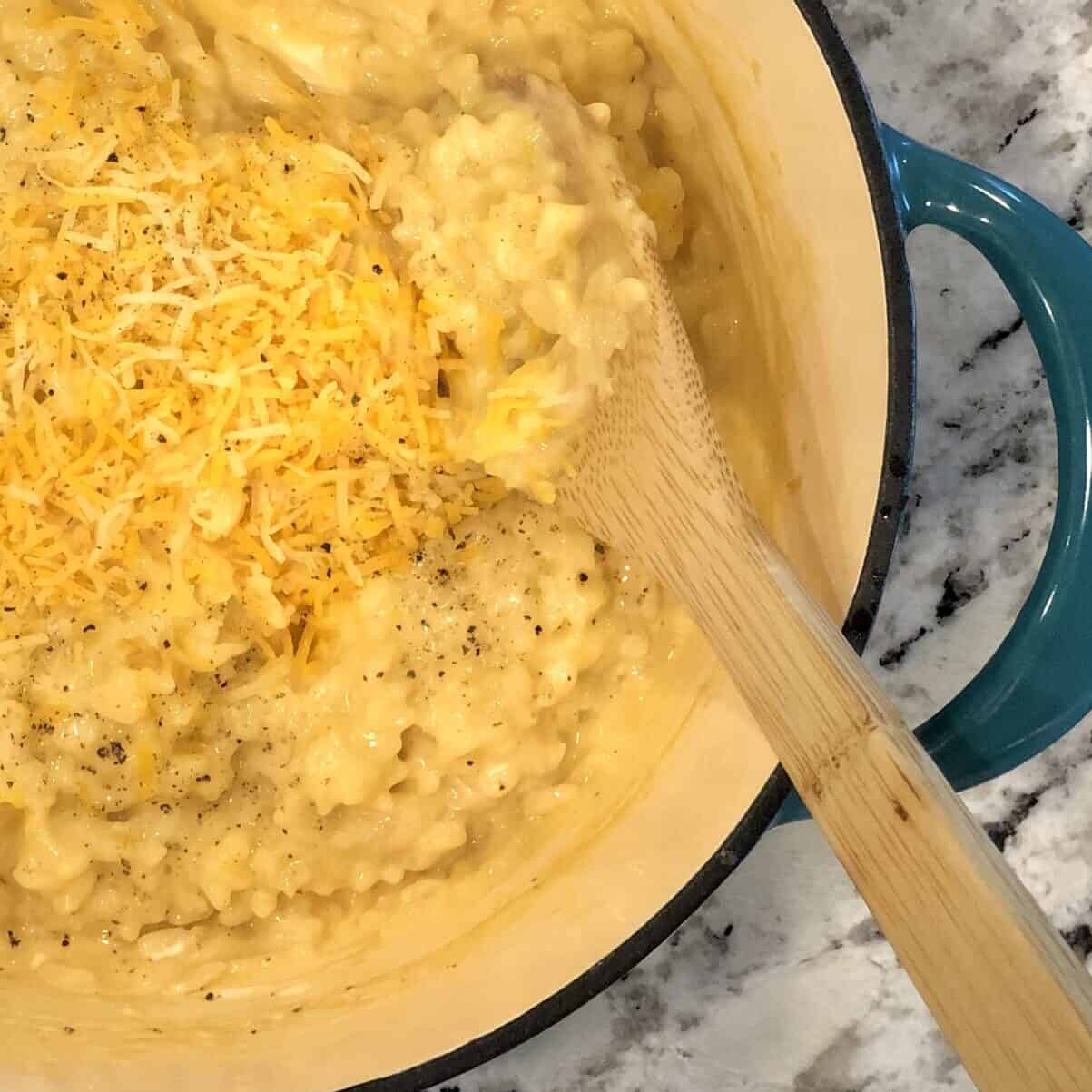 teal pot with cheesy cooked risotto and extra cheese on top on counter top next to a black cutting board