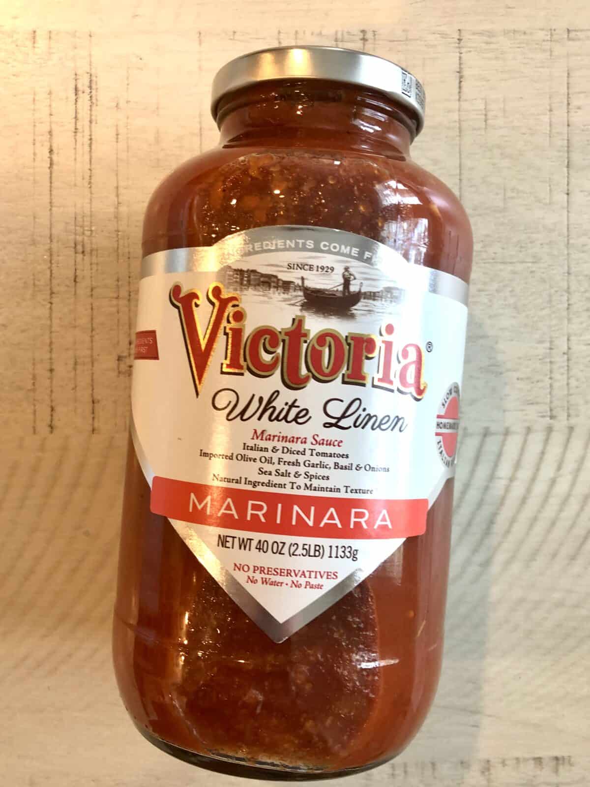 A jar of victoria white linen marinara sauce on a cream colored table