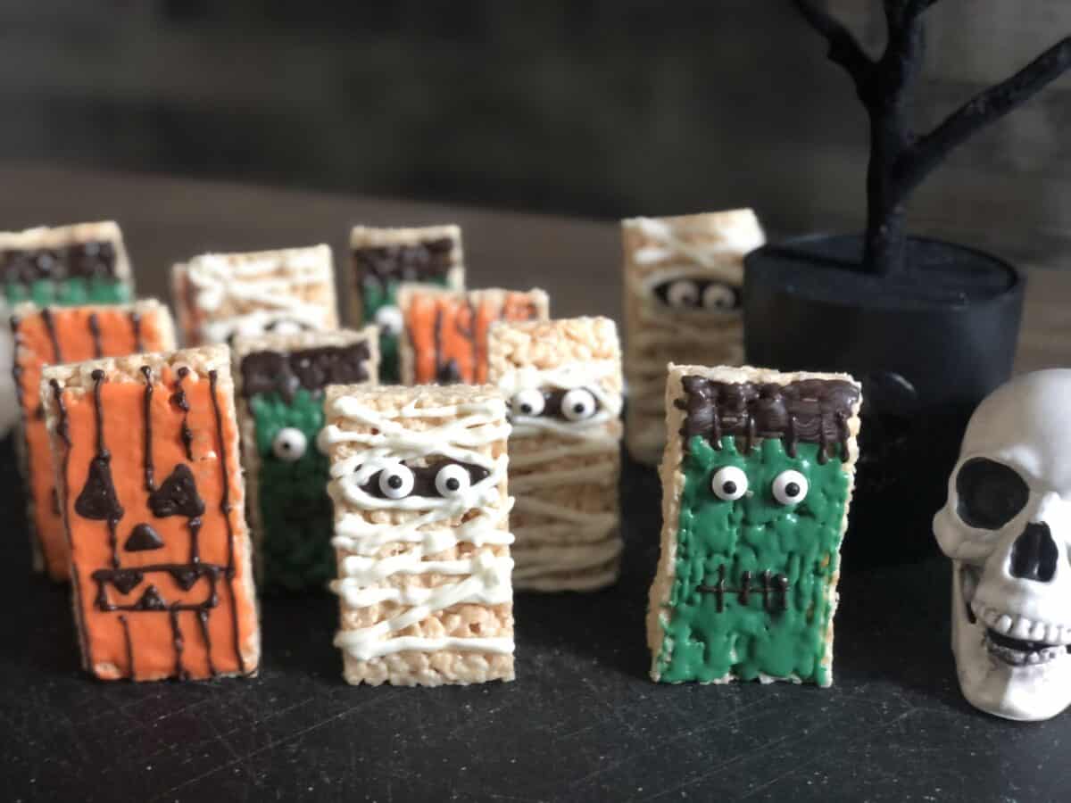 12 rice krispie treats standing up decorated to look like a mummy frankenstein and jack-o-lantern
