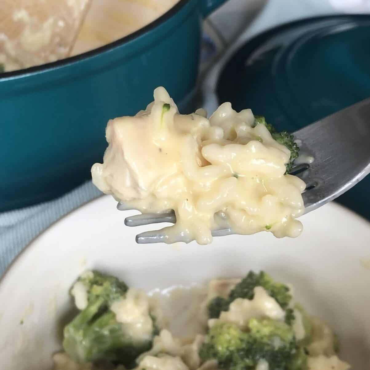 A forkful of risotto with chicken and a bowl of chicken and broccoli risotto with a teal pot in the background