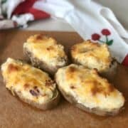 a brown cutting board with 4 easy twice baked potatoes topped with melted cheese and an apron in the backround