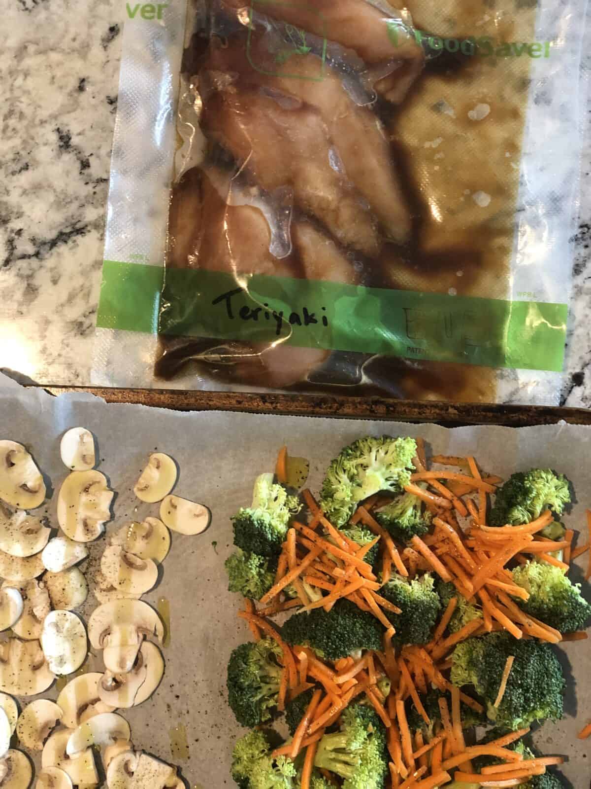a vacuum sealed package of teriyaki freezer friendly chicken marinade and a sheet pan with sliced mushrooms broccoli florets and shredded carrots on parchment paper