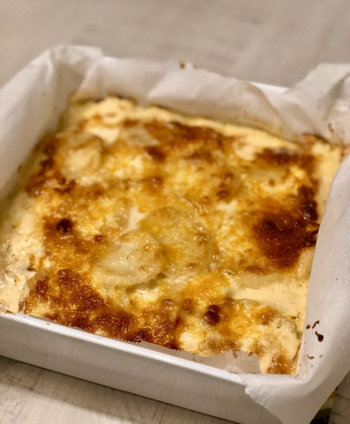 white baking dish with four ingredient au gratin potatoes that has a browned and melted cheese topping