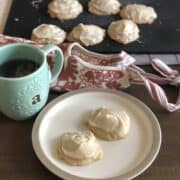 small plate with two frosted apple butter and cardamom cookies with a pink apron and more frosted cookies on a black cutting board