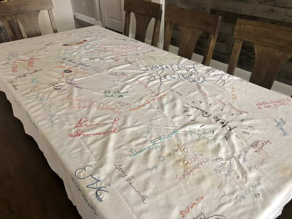 Large dining table with an old signature table cloth spread out with many names sewn on it