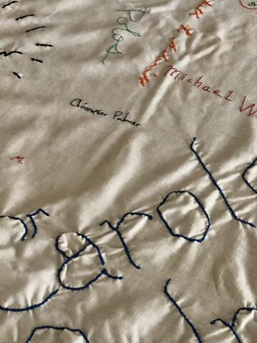A white signature table cloth with the name carole showing in blue embroidery and smaller signatures behind it
