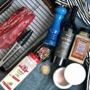 ingredients for a beeftenderoin and red wine sauce including a beef tenderloin on a sheet pan with wire rack and tongs onion powder better than bouillon a blue pepper grinder garlic powder salt jar and bottle of kirkland signature red blend