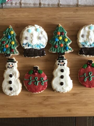 8 christmas rice krispie treats on a wood cutting board decorated to be a christmas tree a snow globe christmas ornament and a snowman