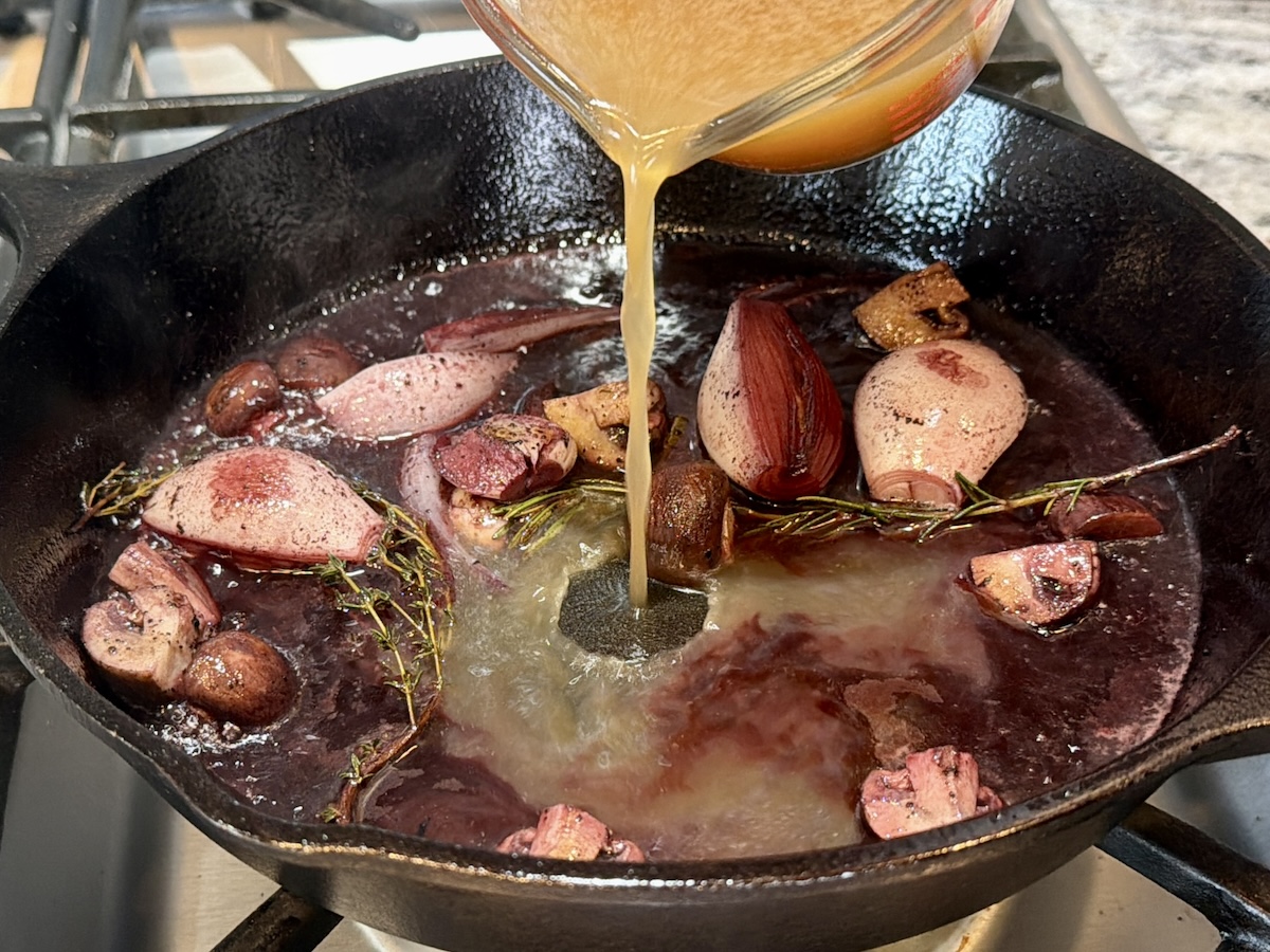 beef stock pouring into cast iron pan of red wine reduction sauce cooking