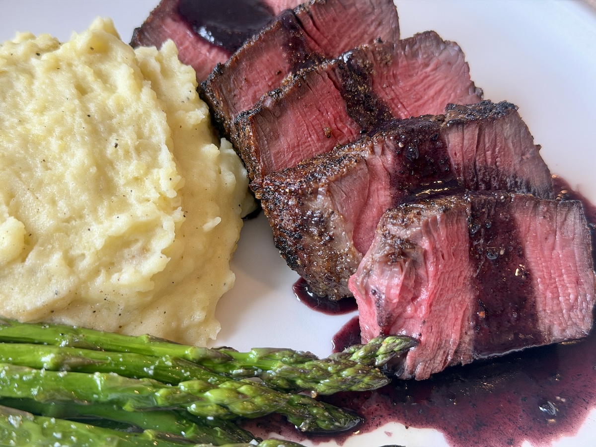 mashed potatoes asparagus sliced steak with red wine sauce on white plate