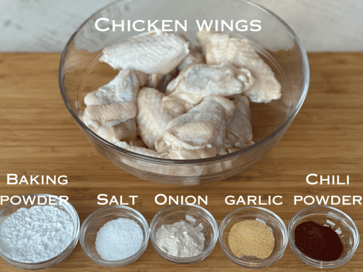raw chicken wings in a glass bowl and small glass bowls of dry spices