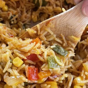 a wood spoon stirring through roasted red pepper and poblano rice