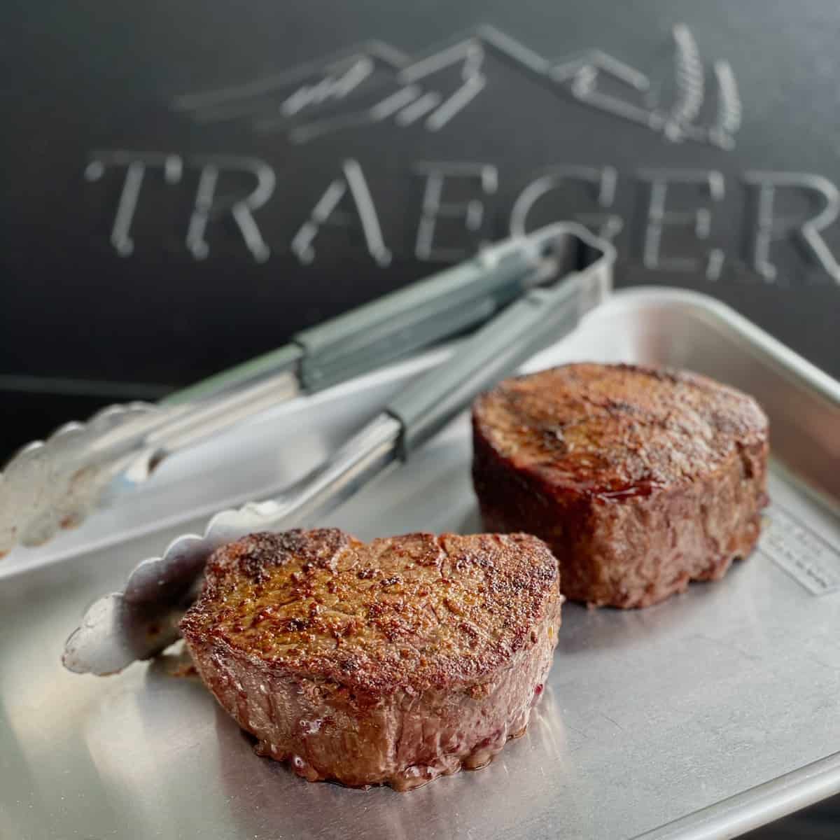 to perfectly cooked filets on a quarter sheet pan with tongs in front of a traeger grill