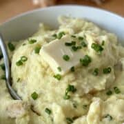 yukon gold mashed potatoes garnished with chives in a white bowl with a silver serving spoon