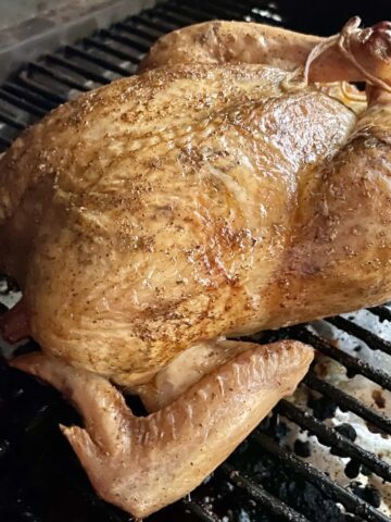 a whole cooked chicken with crispy brown skin on the grate of a traeger grill