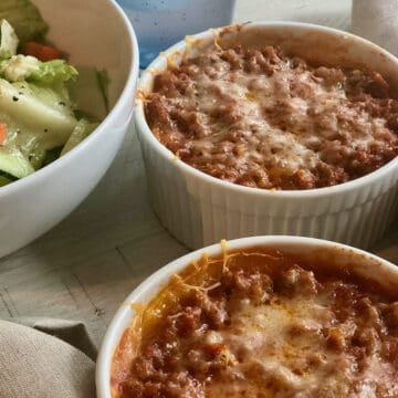 two individual servings of butternut squash lasagna in white ramekins next to a white bowl of green salad