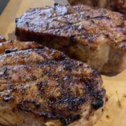 two grilled pork chops with charred grill lines on a brown cutting board