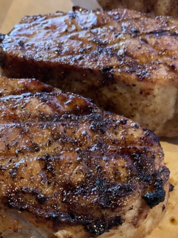 two grilled pork chops with charred grill lines on a brown cutting board