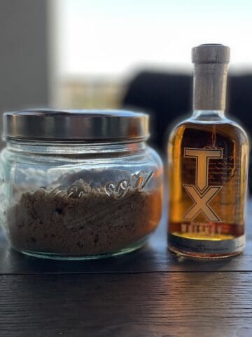a large glass container with lid of brown sugar and a bottle of TX whiskey on a patio table outside