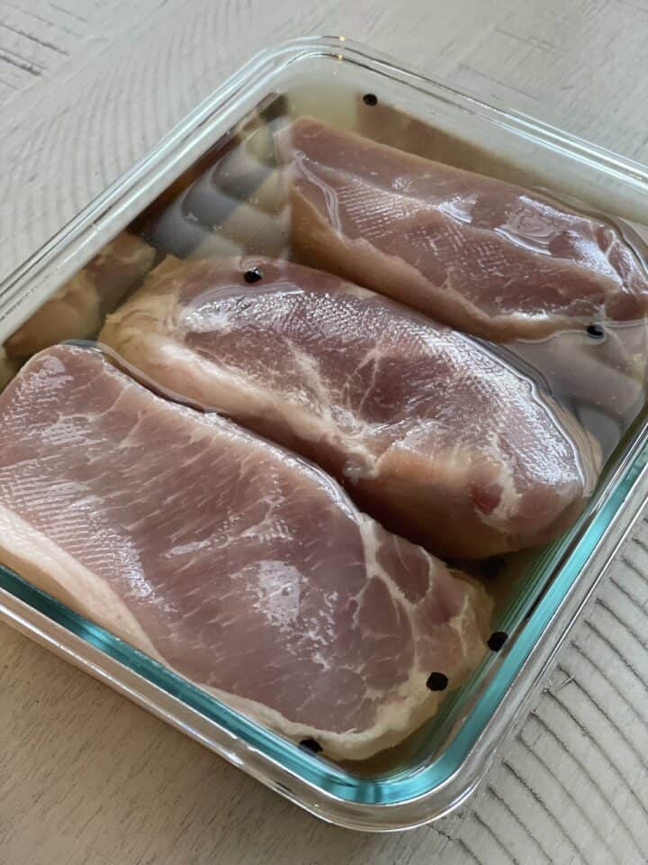 three pork chops submerged in a brine in a large glass snap ware container