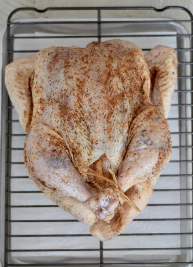 whole raw chicken laying on a sheet pan with a wire rack and seasoned with traeger grill seasoning