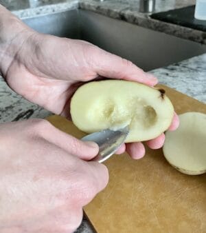 a russet potato cut in half being scooped out with a grapefruit spoon