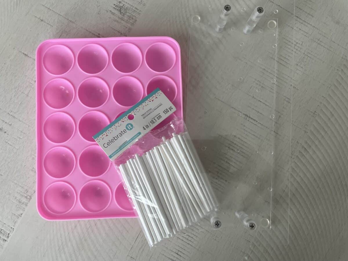 a pink cake pop silicone mold next to 4" lollipop sticks and a clear plastic stand for holding cake pops after they have been dipped in chocolate