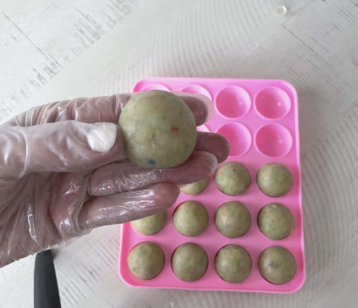 a gloved hand holding a perfectly round and smooth ball of cake