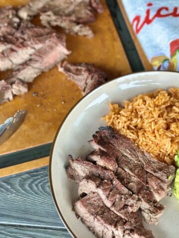 sliced carne asada red rice avocado on tan plate meat on brown cutting board Mexican apron