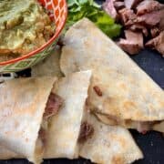 carne asada quesadillas on a large platter with a bowl of guacamole cilantro and extra carne asada