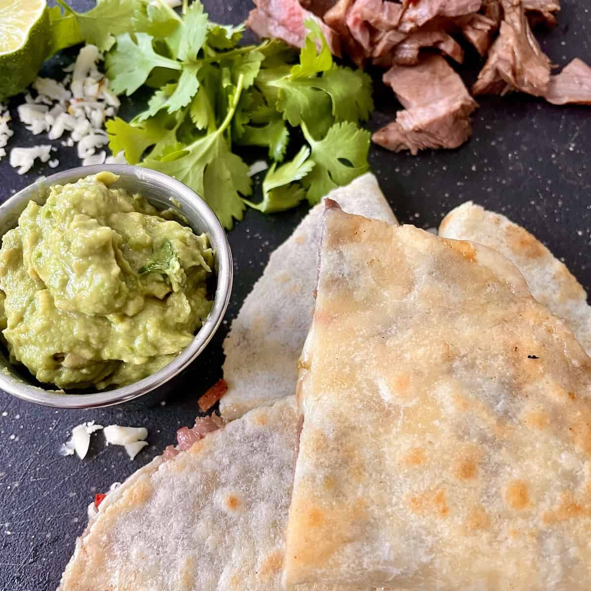 carne asada quesadillas served on a large platter with fresh guacamole steak shredded pepper jack cheese and cilantro for garnish 