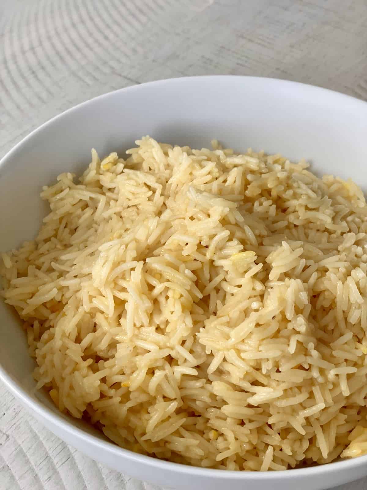 a white bowl on a white table filled with cooked saffron rice that is golden yellow in color