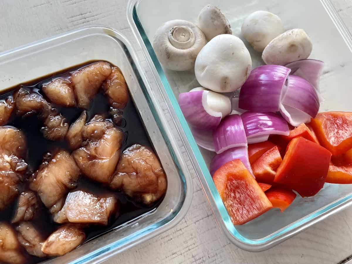 two glass containers one with chunks of marinating chicken in teriyaki sauce and a second container of mushrooms red onion and bell pepper ready for traeger chicken kabobs