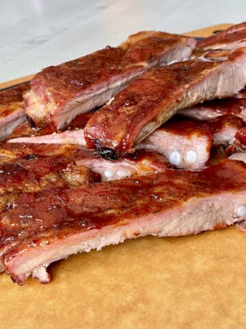 a large pile of saucy cooked st louis ribs off the traeger grill on a large brown cutting board