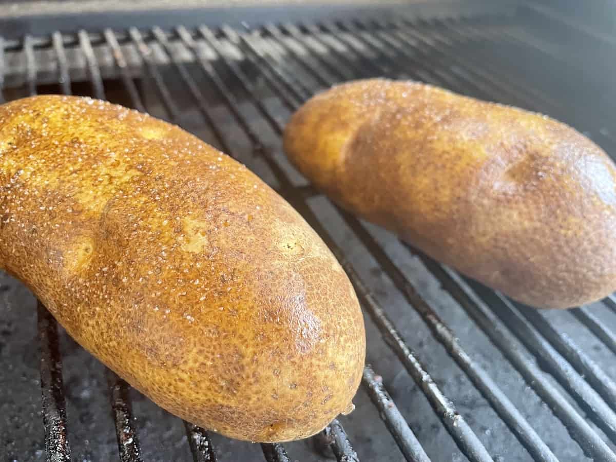 two traeger baked potatoes sitting on the grill grate of a traeger grill