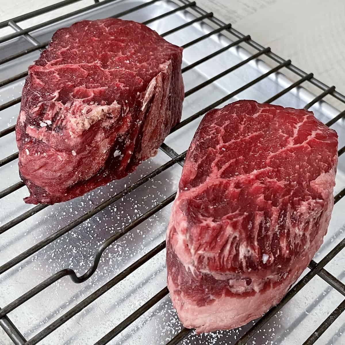 two dry aged beef tenderloin filets showing a bright red color from aging in salt overnight on a sheet pan with a wire rack 