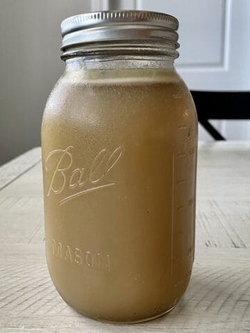 jar of chilled homemade chicken stock on a white kitchen table with a black chair in the background