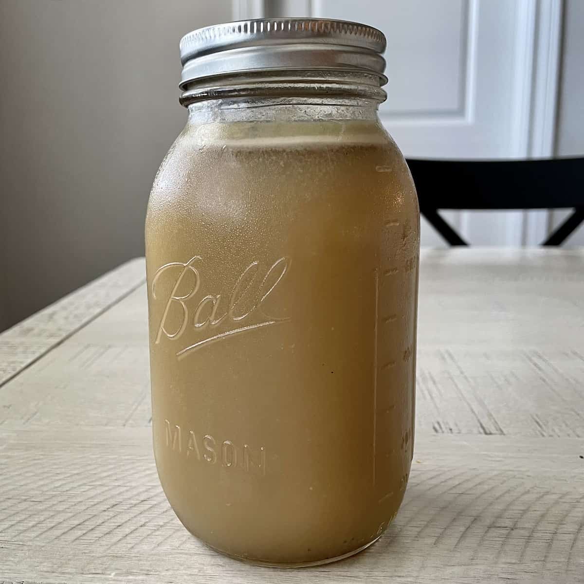 jar of chilled homemade chicken stock on a white kitchen table with a black chair in the background