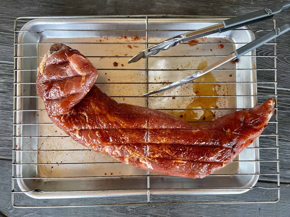 a seasoned and uncooked pork tenderloin on a sheet pan lined with a wire rack