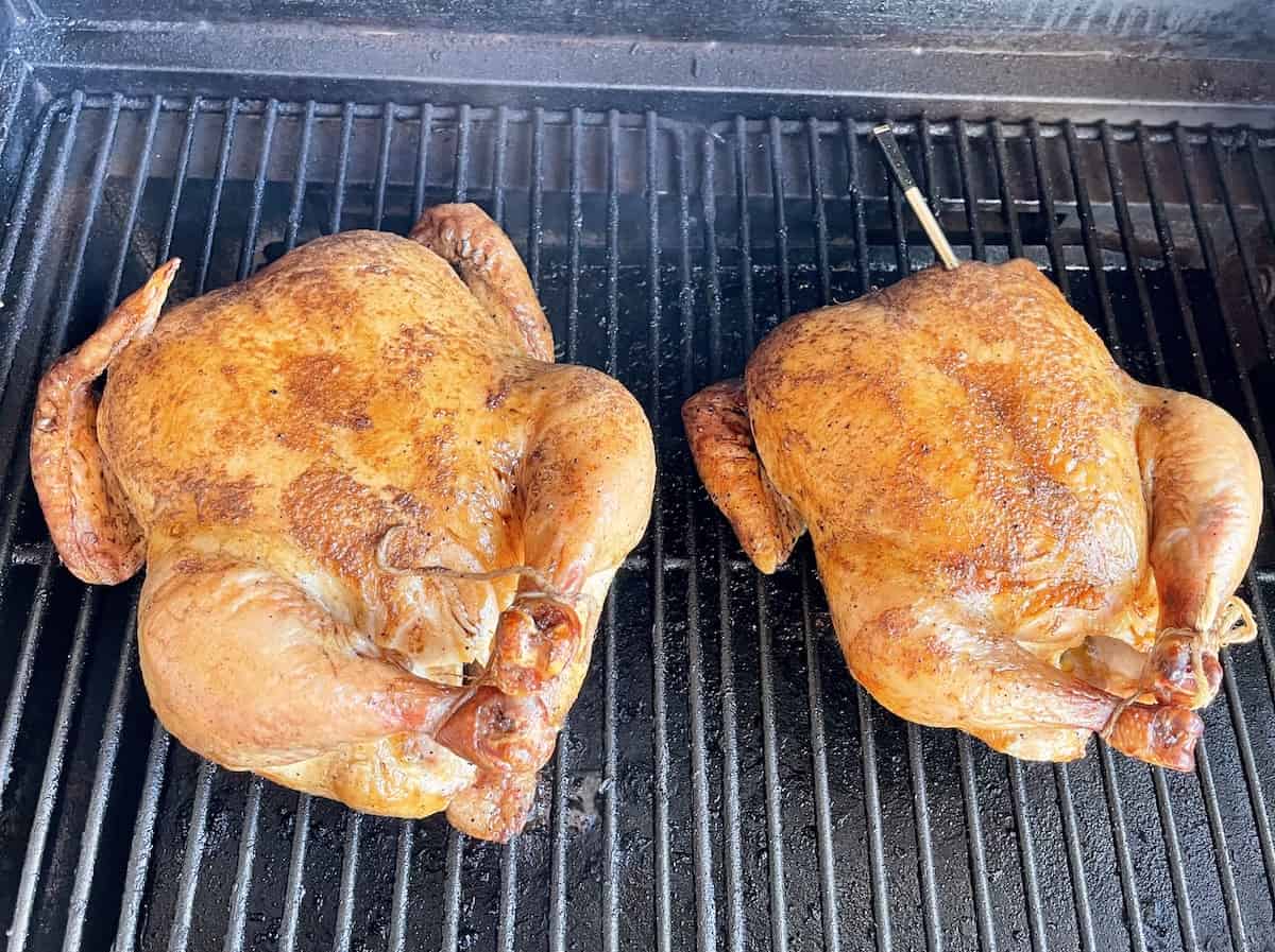 two whole chickens on a traeger cooking with a wireless meat thermometer in the chicken on the left