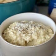 a light brown bowl filled with cacio e pepe risotto and freshly grated parmesan cheese and cracked black pepper
