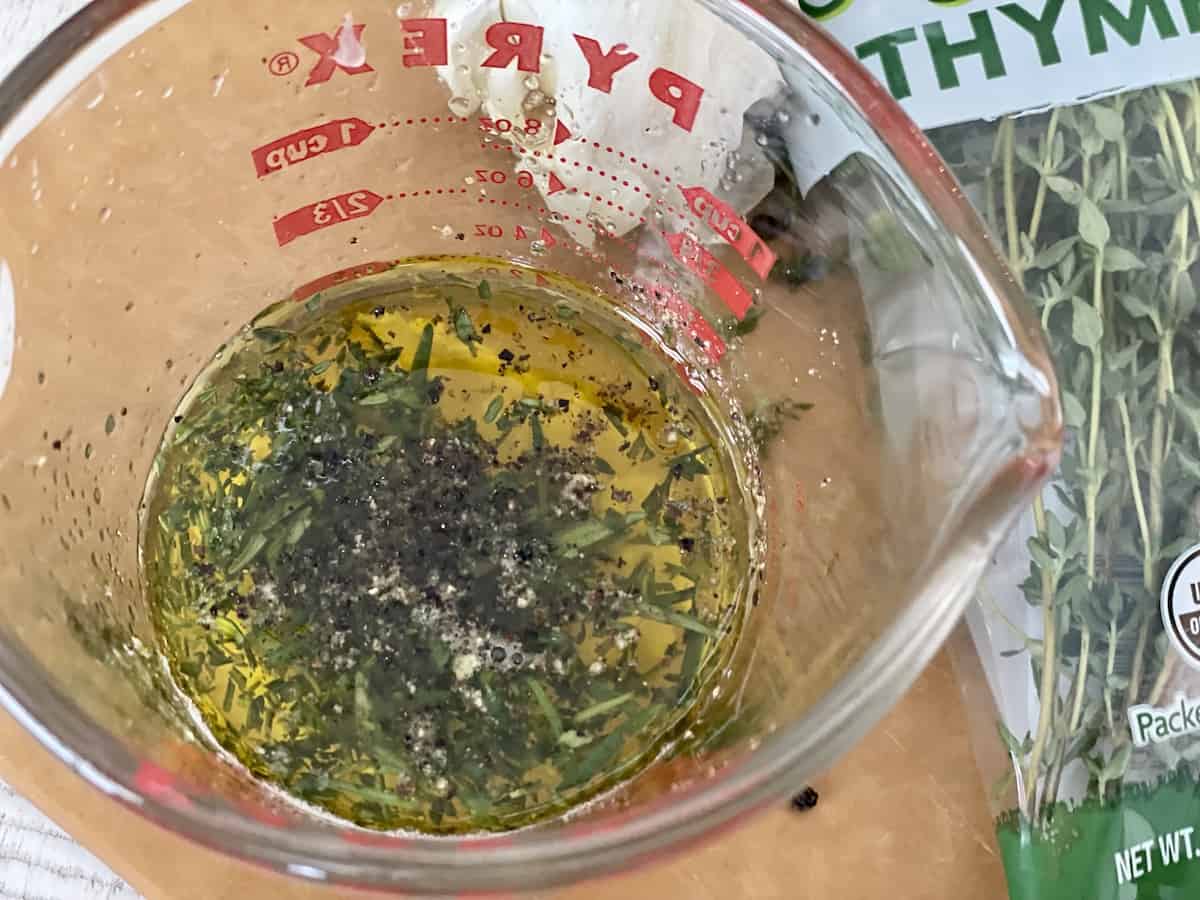 glass measuring cup of lemon and herb marinade on a brown cutting board with fresh thyme next to it